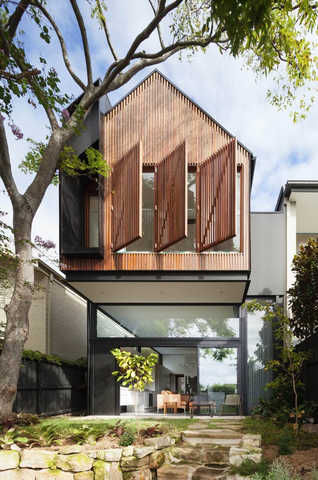 A modern wooden structure with a geometric facade and large glass windows overlooking a lush garden.