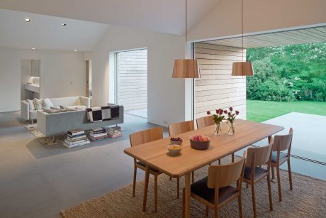 Minimalist open-plan living area with wooden dining table, pendant lamps, and garden view.