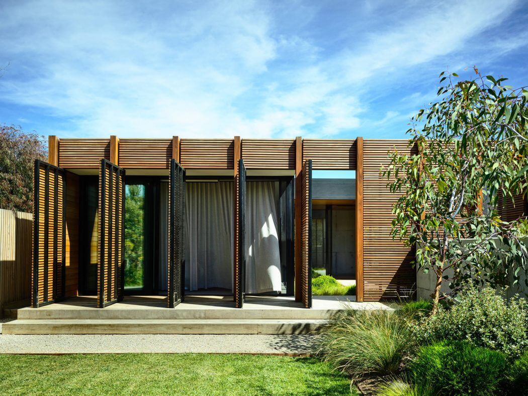 Sleek, modern structure with wooden slat façade and expansive glass doors opening to lush greenery.