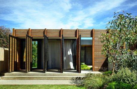 Sleek, modern structure with wooden slat façade and expansive glass doors opening to lush greenery.