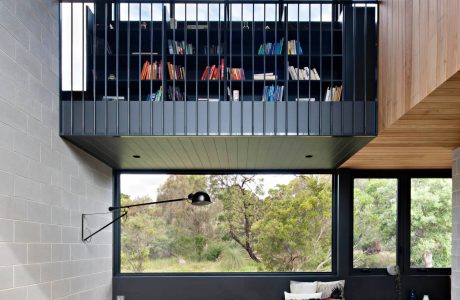 A modern living space with a wall-mounted bookshelf, large windows, and a wooden coffee table.