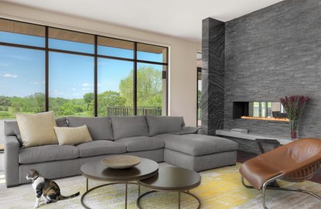 Spacious modern living room with floor-to-ceiling windows, gray sectional, and stone fireplace.