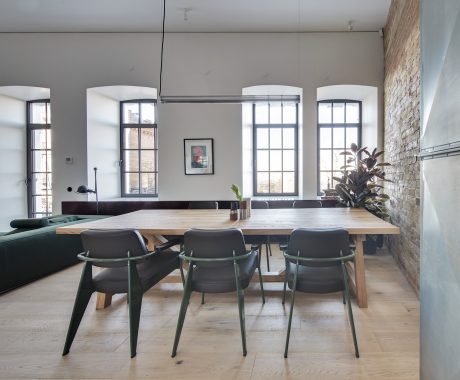 Spacious loft-style dining area with large windows, wooden table, and minimalist decor.