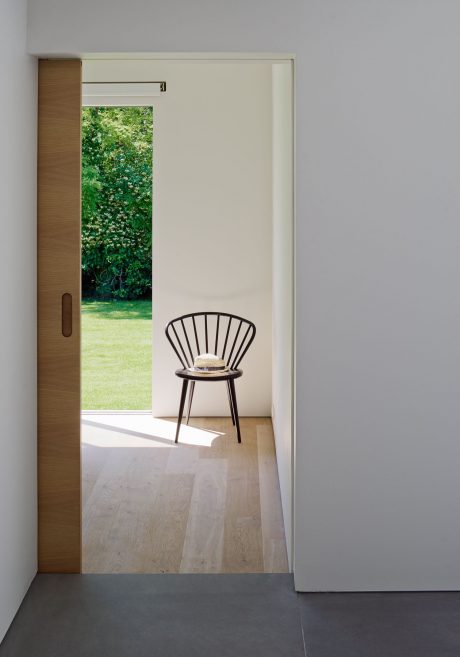 A sparsely furnished room with a simple wooden chair in the foreground, overlooking a lush green outdoor scene.