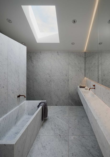A modern bathroom with sleek marble surfaces, a skylight, and minimalist fixtures.