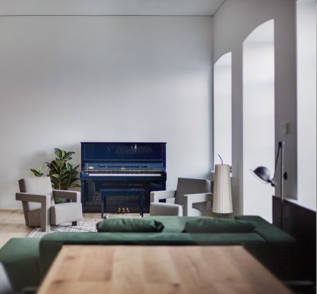 A modern room with a blue upright piano, green couch, and minimalist furniture.