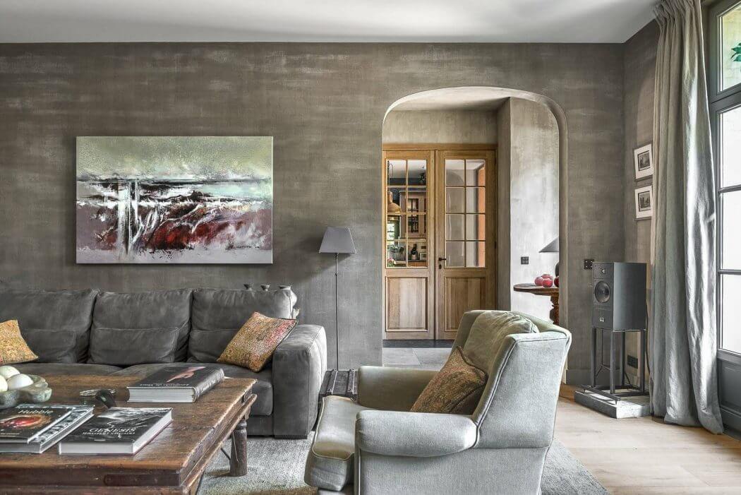 A cozy living room with a large gray sofa, wooden accents, and an arched doorway leading to another room.
