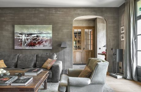 A cozy living room with a large gray sofa, wooden accents, and an arched doorway leading to another room.