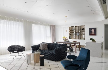 A spacious modern living room with sleek furniture, cozy textures, and a shelving unit.