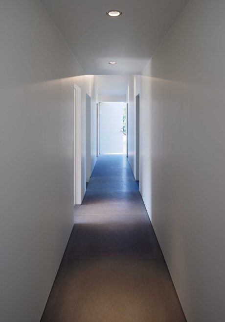 Minimalist hallway with recessed lighting, white walls, and dark hardwood floors.
