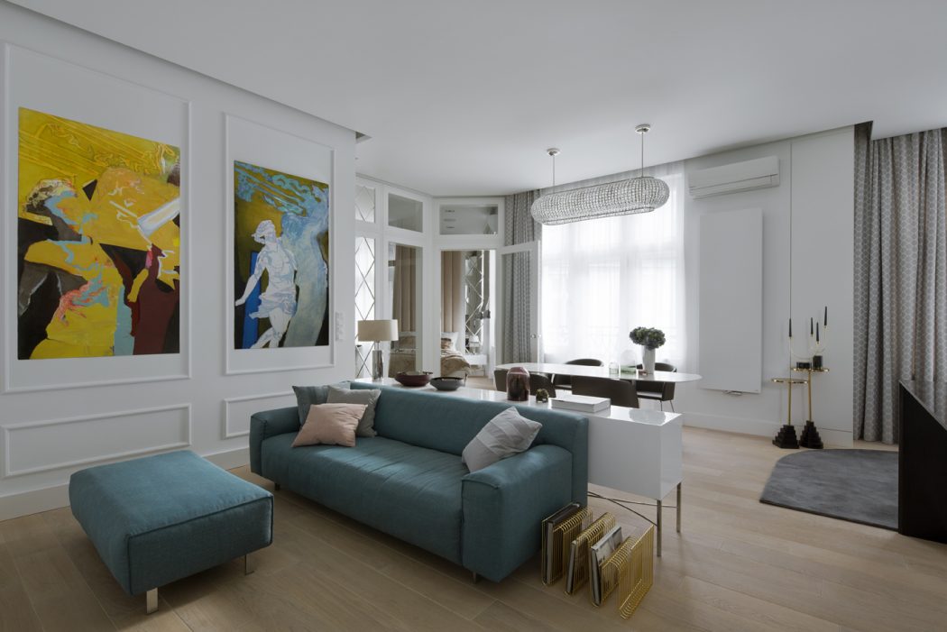 Spacious modern living room with plush blue sofa, colorful artwork, and chic lighting fixtures.