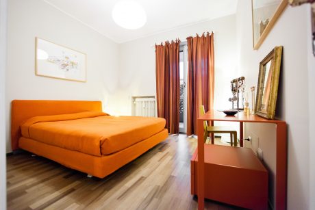Warm-toned bedroom with plush orange bed, curtains, and wooden furniture accents.