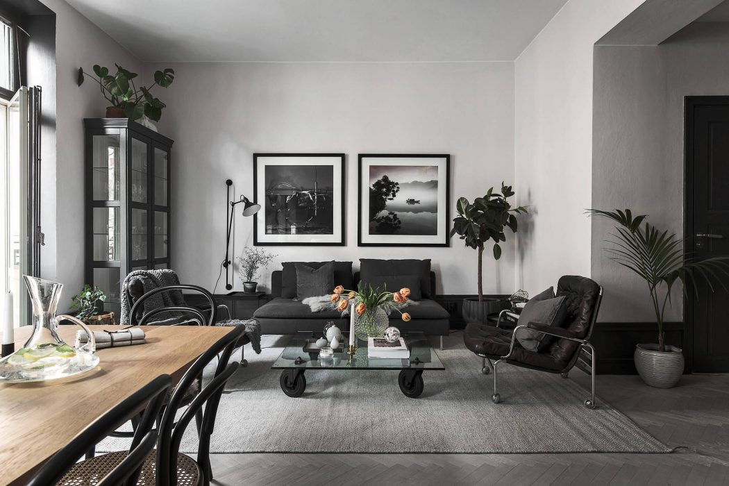 A stylish, modern living room with dark furniture, framed artwork, and potted plants.