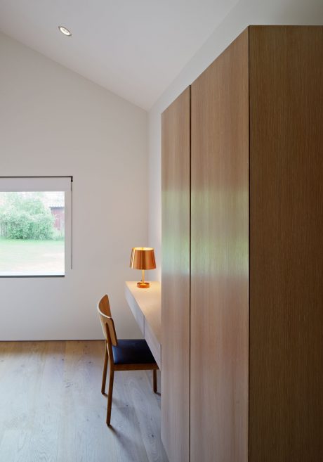 Minimalist room with wooden built-in wardrobe, chair, and table lamp providing subtle lighting.