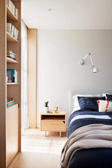 Cozy bedroom with wooden bookshelf, modern nightstand, and comfortable bedding.