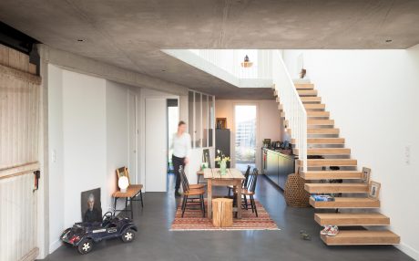 Spacious, open-concept living area with concrete walls, wooden stairs, and minimalist furnishings.