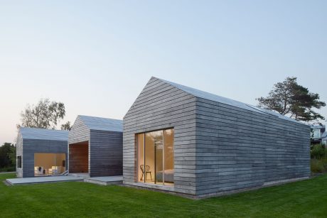 Modern, minimalist architecture with slanted gray slate roof and glass walls amid a grassy landscape.