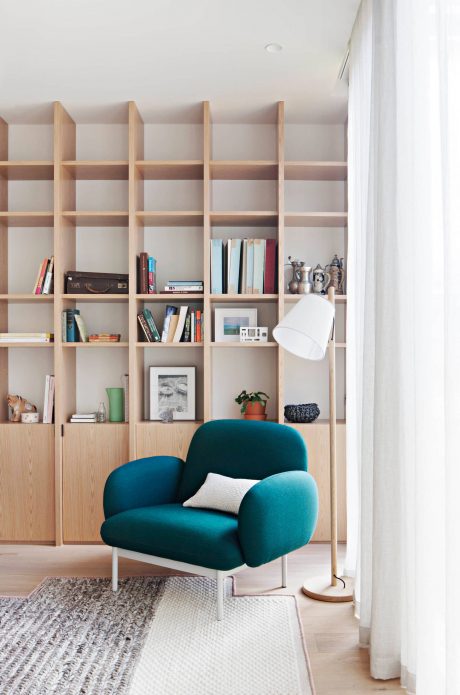 A cozy living room with a plush teal armchair, built-in shelving, and a minimalist floor lamp.