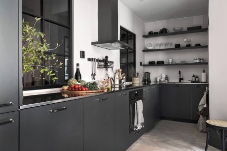 A modern, minimalist kitchen with sleek black cabinets, open shelves, and a large window.
