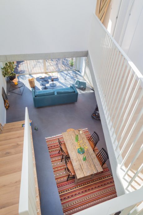 Minimalist open-concept interior with patterned rug, wood table, and teal sofa.