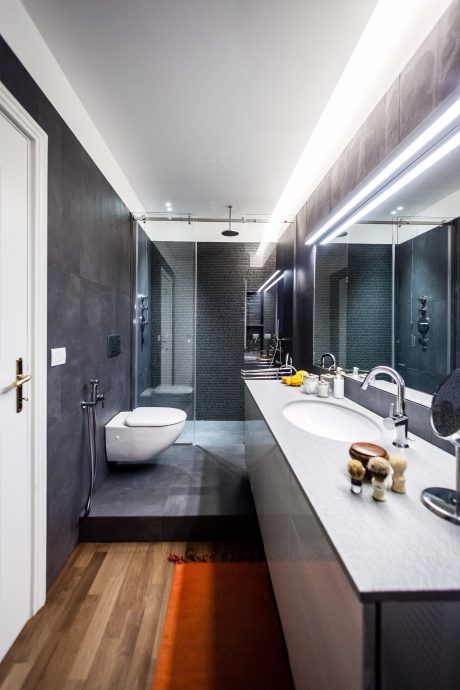 A modern, minimalist bathroom with sleek black tiles, a large vanity, and a minimalist toilet.