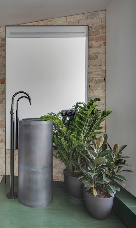 A modern bathroom design with a neutral color scheme, brick wall, and lush potted plants.