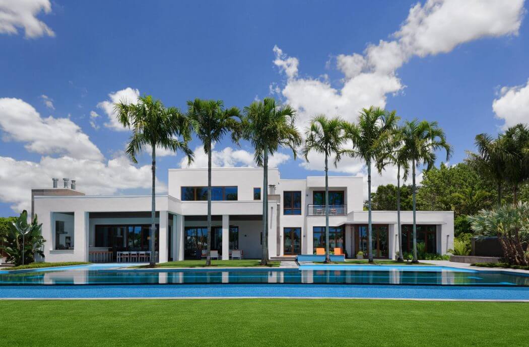 Modern tropical villa with expansive windows, pool, and lush palm trees.