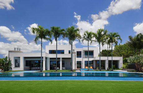 Modern tropical villa with expansive windows, pool, and lush palm trees.