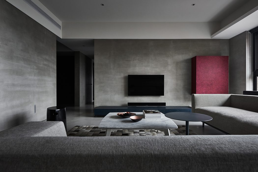 Minimalist living room with concrete walls, black furniture, and a vibrant pink accent.