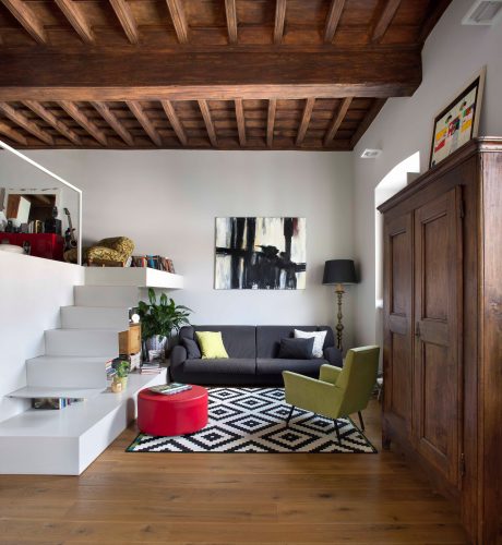 A cozy living room with a wooden beamed ceiling, gray sofa, and patterned area rug.