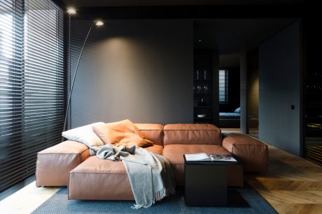 A modern living room with a large, plush leather sofa, wood floor, and window blinds.