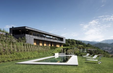 A modern, two-story building with a sleek, black facade overlooking a grassy hillside and swimming pool.