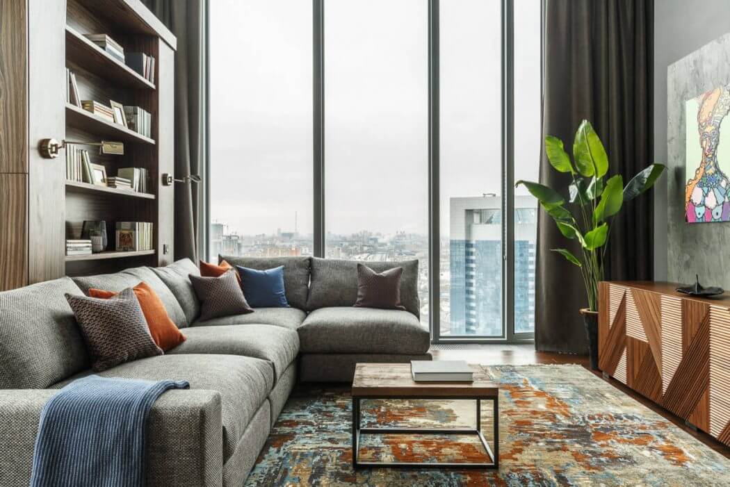 Sleek modern interior with large windows, plush grey sofa, and wooden shelving unit.