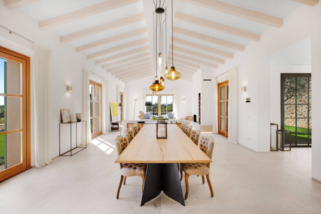 Spacious, bright dining room with exposed wooden beams, pendant lights, and plush chairs.