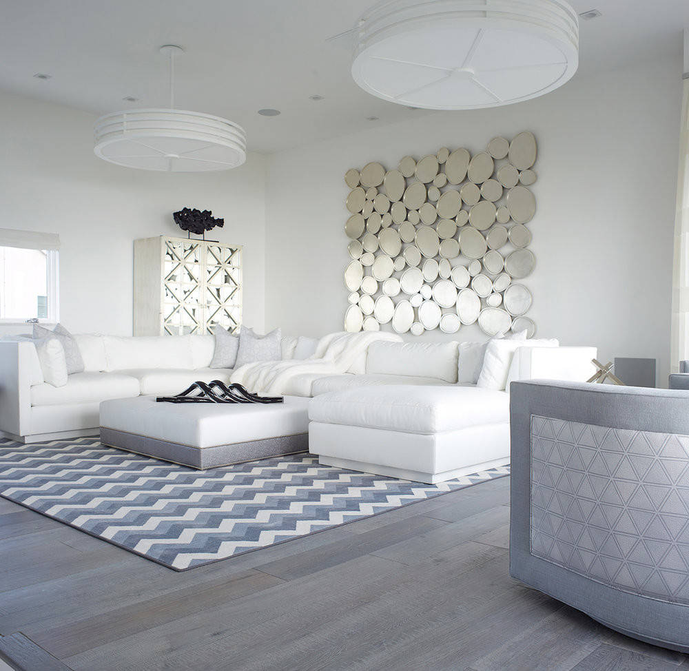 Sleek, modern living room with white sofas, circular mirror installation, and geometric rug.