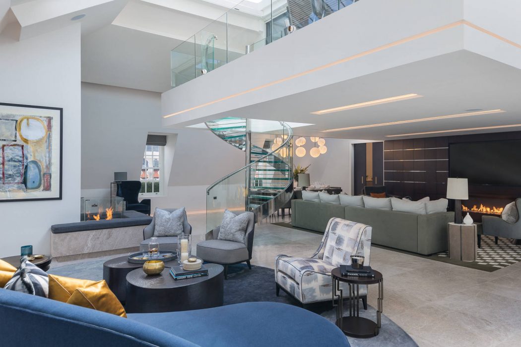 Luxurious contemporary living area with glass staircase, sleek furnishings, and statement lighting.