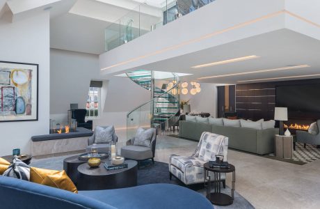 Luxurious contemporary living area with glass staircase, sleek furnishings, and statement lighting.