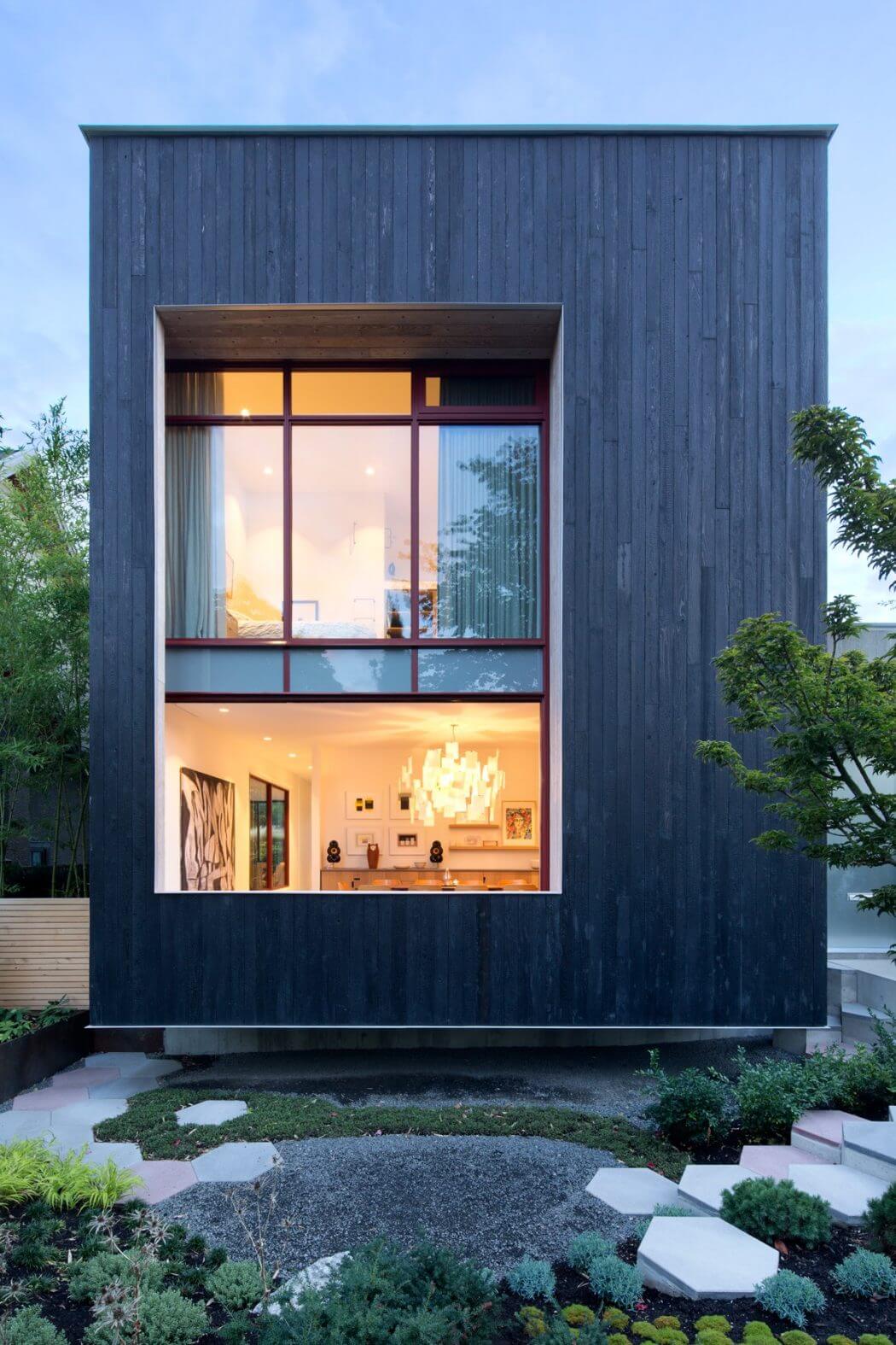 A modern, minimalist house with wooden exterior and large glass windows showcasing the interior.