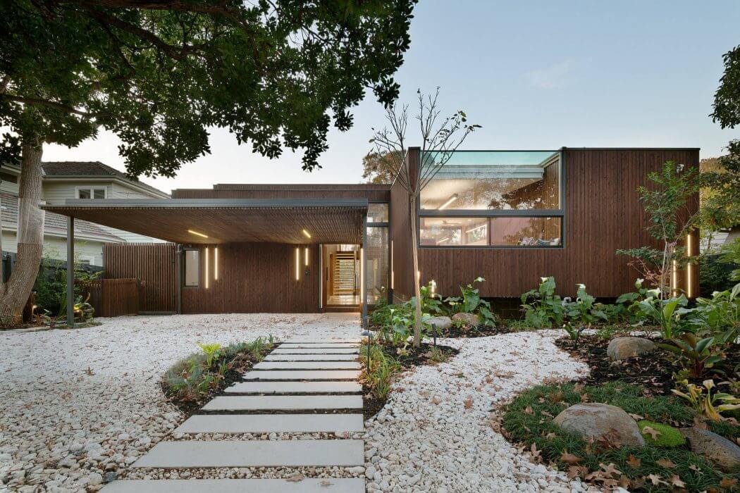 A modern, wooden-clad residence with a covered entryway and lush landscaping.