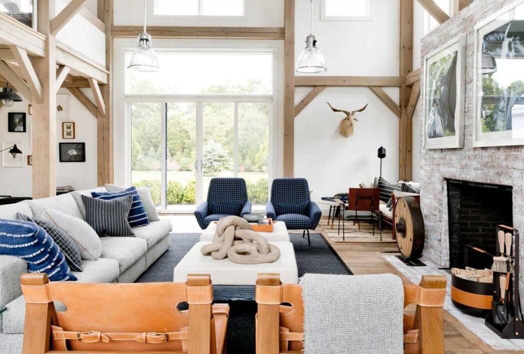 Rustic, open-concept living room with timber frame, large windows, and cozy furnishings.