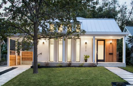 A modern, single-story house with a metal roof, large windows, and a wooden entry door.