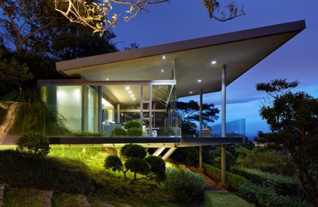 Contemporary mountain retreat with floor-to-ceiling glass walls, sleek roofline, and lush landscaping.