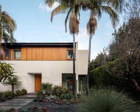 A modern, two-story residence with wooden accents, surrounded by lush tropical vegetation.