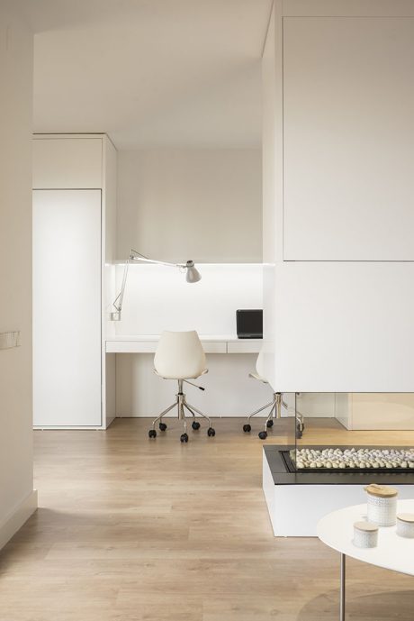 Minimalist office space with sleek white furniture, built-in storage, and natural lighting.