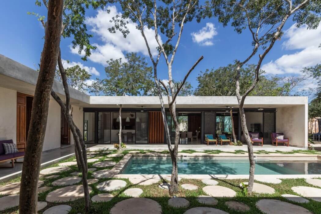 Modern single-story residence with a pool, patio, and lush vegetation surrounding it.