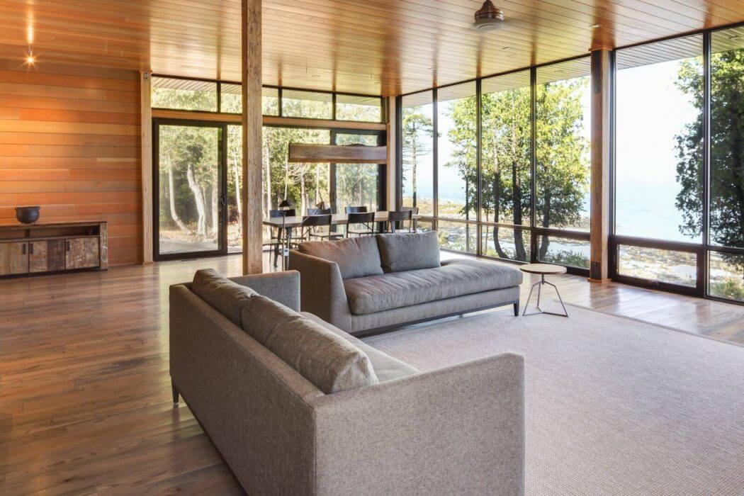 Spacious modern living room with floor-to-ceiling windows, wooden accents, and plush gray sofas.