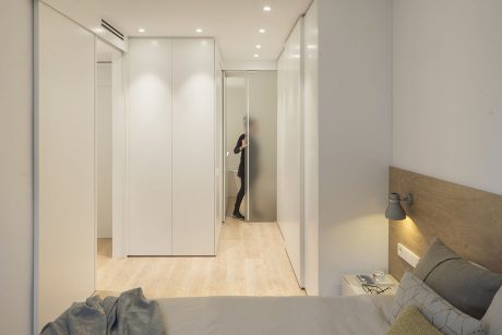Bright, minimalist bedroom with neutral colors, recessed lighting, and built-in closets.