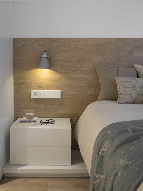 Cozy bedroom with warm wood paneling, bedside table, and modern lighting fixture.