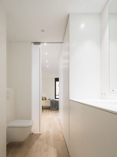 Well-lit hallway with minimalist design, leading to a bedroom with wood floor and neutral decor.