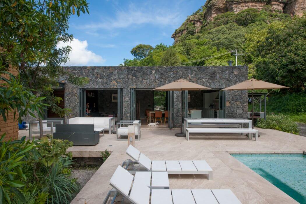 A modern outdoor living space with a stone wall, covered seating areas, and a pool.